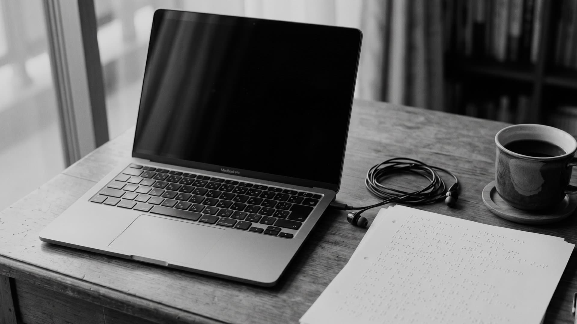 仕事机の上に置かれたPC、点字用紙。コーヒーのマグカップ。