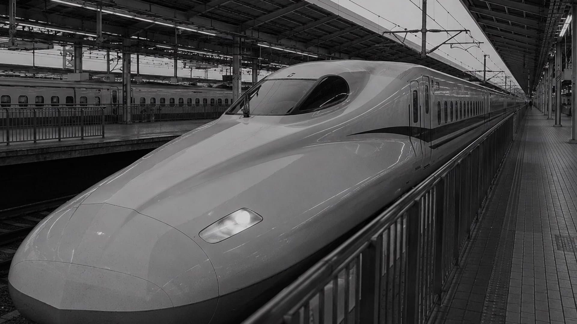 駅のホームに停車する新幹線の先頭車両。流線型のノーズを正面近くから捉えた。モノクロ写真。